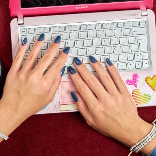 Mãos no notebook e caixa de CD com esmalte cor Jeans de Colorama Retrô.